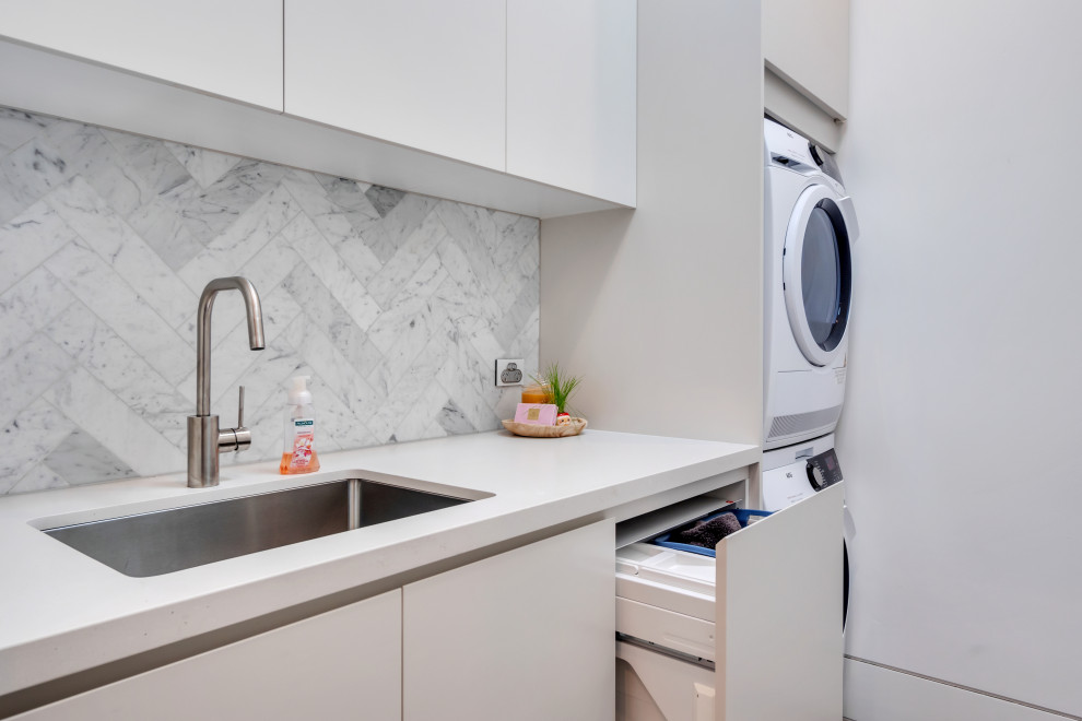 This is an example of a contemporary single-wall laundry room in Sydney with flat-panel cabinets, white walls, a stacked washer and dryer, white benchtop, white cabinets and quartz benchtops.