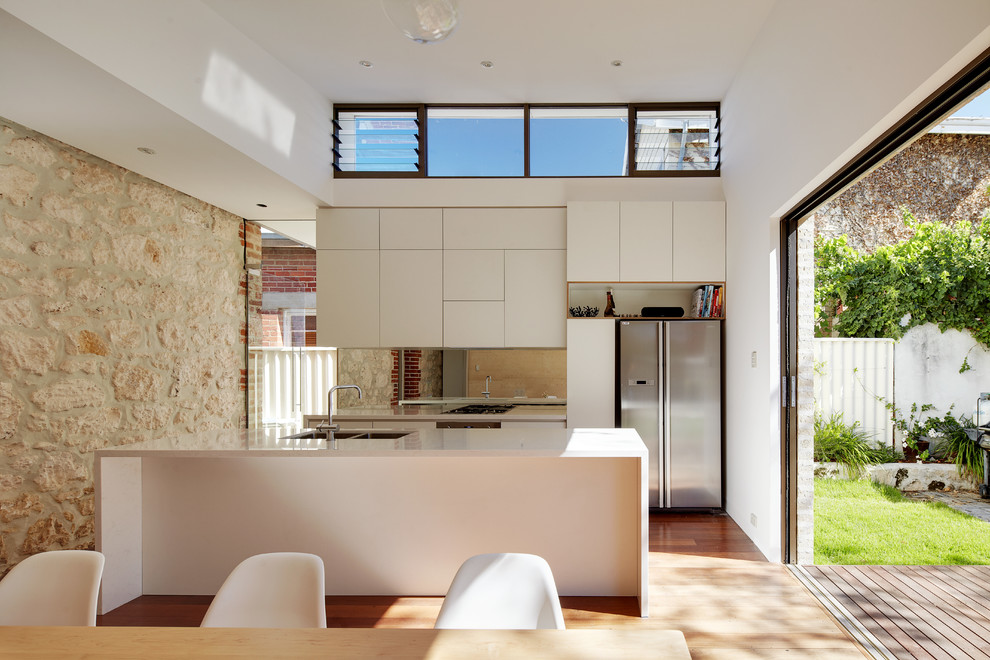 This is an example of a small contemporary galley eat-in kitchen in Perth with an undermount sink, solid surface benchtops, glass sheet splashback, stainless steel appliances, medium hardwood floors, with island, flat-panel cabinets and white cabinets.