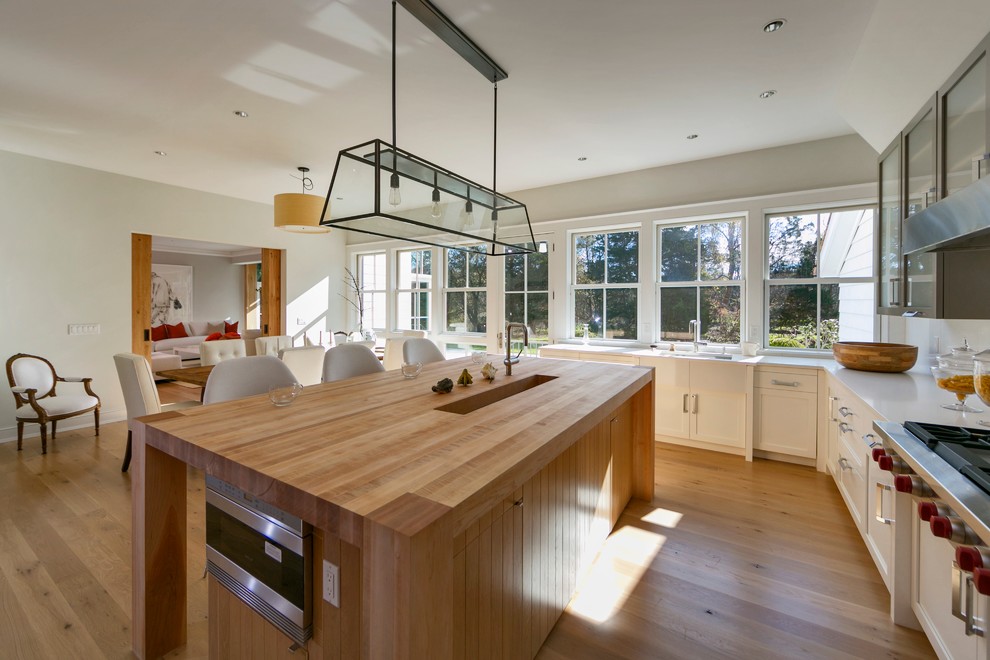 Inspiration for a mid-sized contemporary l-shaped eat-in kitchen in New York with wood benchtops, a farmhouse sink, shaker cabinets, white cabinets, stainless steel appliances, white splashback, light hardwood floors and with island.