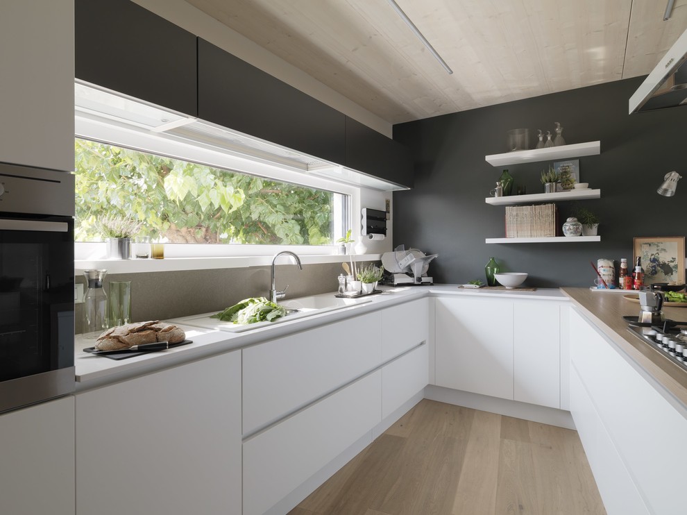 Design ideas for a mid-sized contemporary u-shaped kitchen in Other with a double-bowl sink, flat-panel cabinets, white cabinets, grey splashback, stainless steel appliances, light hardwood floors and a peninsula.