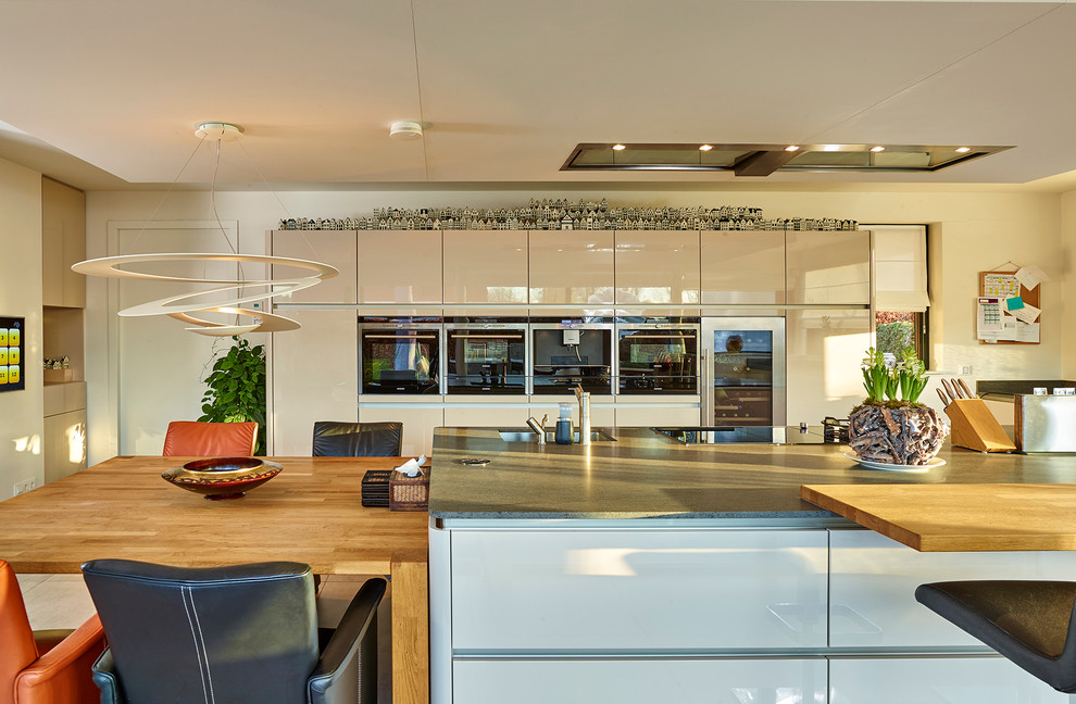 This is an example of a large contemporary single-wall eat-in kitchen in Other with an integrated sink, flat-panel cabinets, beige cabinets, quartz benchtops, black appliances, travertine floors and with island.