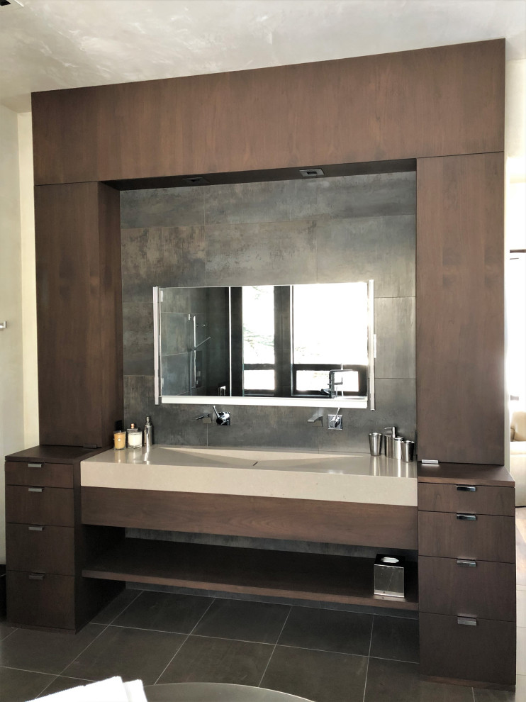 This is an example of a mid-sized contemporary master bathroom in Other with flat-panel cabinets, dark wood cabinets, a freestanding tub, a curbless shower, gray tile, beige walls, a trough sink, brown floor, a hinged shower door, beige benchtops, an enclosed toilet, a double vanity and a built-in vanity.