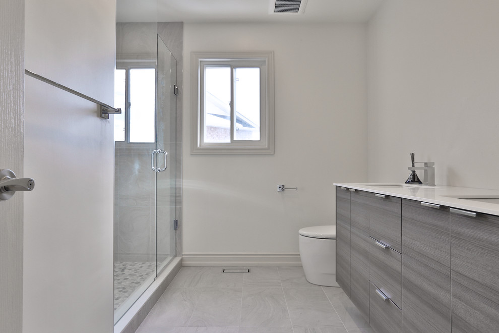 Inspiration for a mid-sized contemporary master bathroom in Toronto with flat-panel cabinets, grey cabinets, an open shower, a one-piece toilet, white tile, stone tile, white walls, porcelain floors, an undermount sink, solid surface benchtops, grey floor and a hinged shower door.