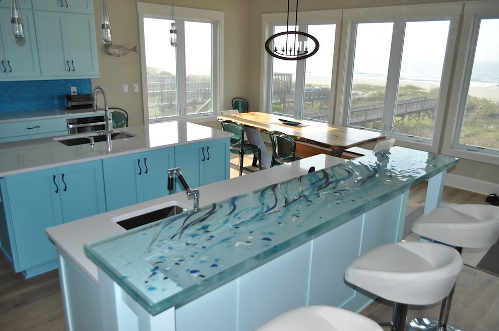 Design ideas for a mid-sized beach style galley eat-in kitchen in Montreal with an undermount sink, shaker cabinets, blue cabinets, glass benchtops, blue splashback, stainless steel appliances, light hardwood floors, no island and turquoise benchtop.