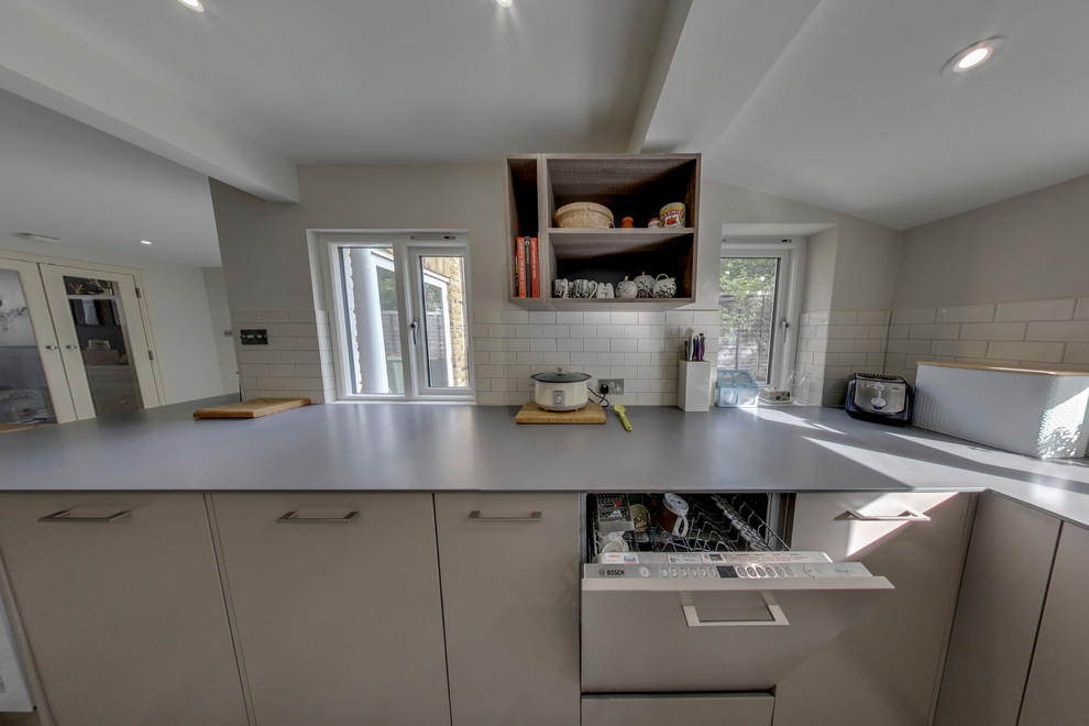 Photo of a mid-sized eclectic galley eat-in kitchen in Surrey with a drop-in sink, flat-panel cabinets, grey cabinets, solid surface benchtops, white splashback, ceramic splashback, panelled appliances, light hardwood floors, no island and grey floor.