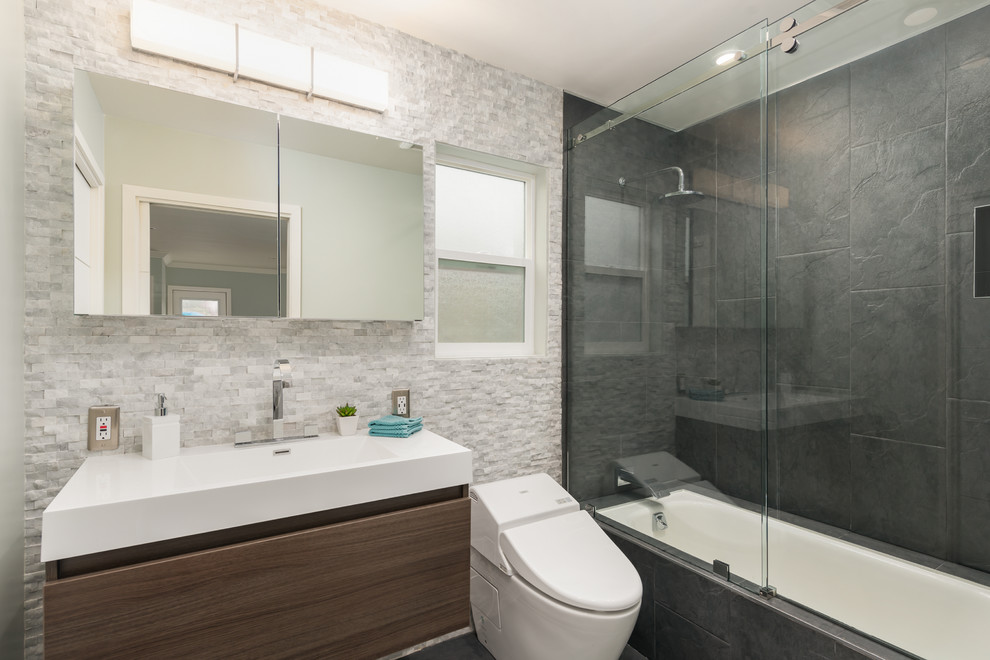 Small modern master bathroom in San Francisco with an integrated sink, flat-panel cabinets, dark wood cabinets, engineered quartz benchtops, a drop-in tub, a shower/bathtub combo, a wall-mount toilet, black tile, cement tile, grey walls and ceramic floors.