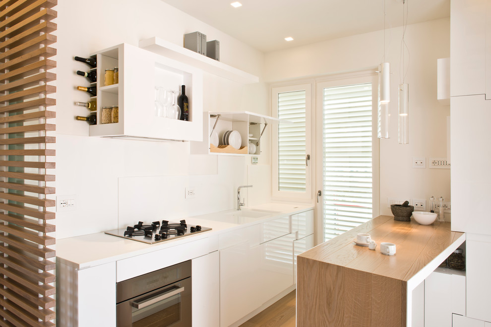 This is an example of a small scandinavian galley kitchen in Rome with an integrated sink, flat-panel cabinets, white cabinets, wood benchtops, white splashback, stainless steel appliances, light hardwood floors and a peninsula.