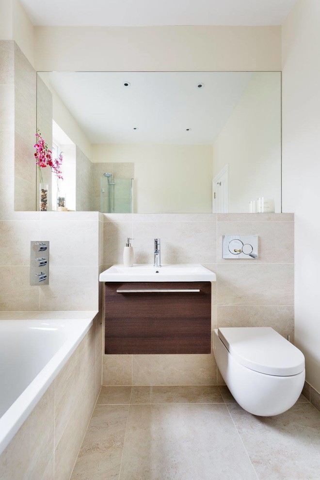 Photo of a modern bathroom in London with a shower/bathtub combo, a wall-mount toilet, beige tile, beige walls and a wall-mount sink.