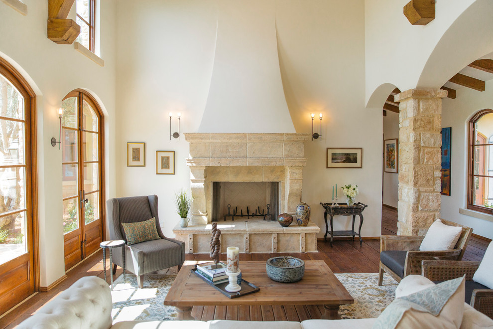 Inspiration for a mediterranean living room in San Diego with white walls, medium hardwood floors, a two-sided fireplace, a stone fireplace surround and brown floor.