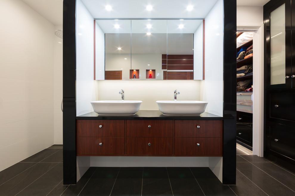 This is an example of a mid-sized contemporary master bathroom in Canberra - Queanbeyan with medium wood cabinets, white walls, a vessel sink, black benchtops, a freestanding tub, an open shower, white tile, ceramic tile, ceramic floors, granite benchtops, multi-coloured floor, an open shower and flat-panel cabinets.