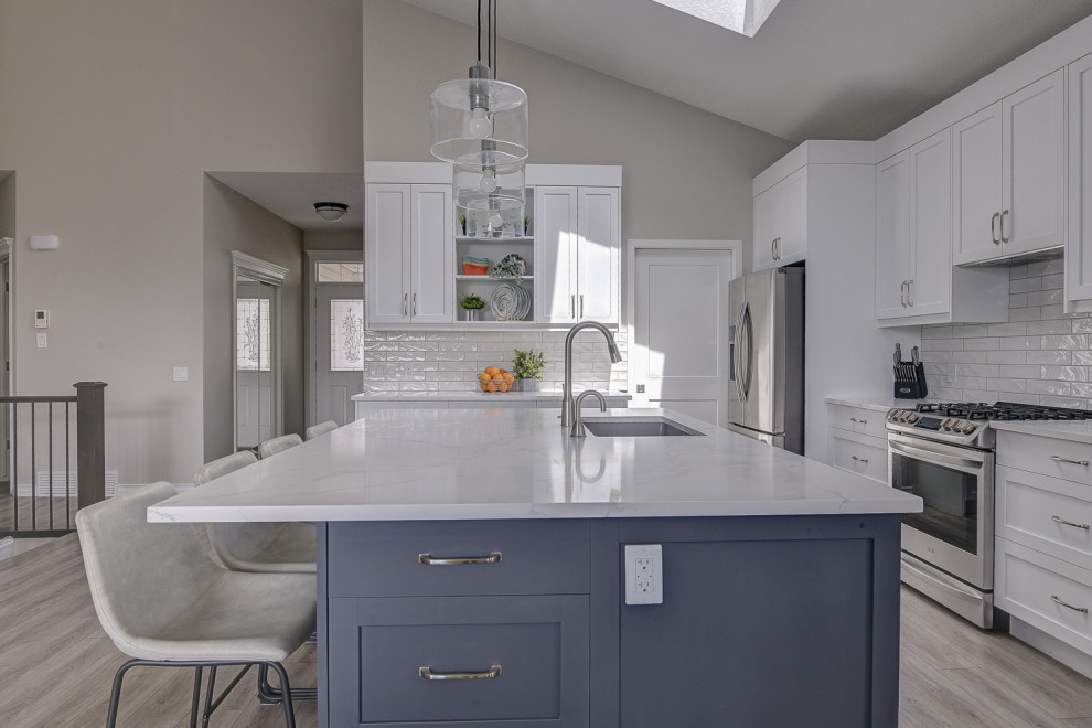 This is an example of a mid-sized transitional l-shaped eat-in kitchen in Calgary with an undermount sink, shaker cabinets, grey cabinets, quartz benchtops, white splashback, subway tile splashback, stainless steel appliances, vinyl floors, with island, grey floor and white benchtop.