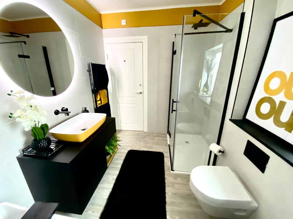 Exemple d'une grande salle de bain tendance pour enfant avec un placard à porte plane, des portes de placard noires, WC suspendus, un carrelage blanc, des carreaux de porcelaine, un mur jaune, sol en stratifié, une vasque, un plan de toilette en verre, un sol marron, un plan de toilette noir, une baignoire indépendante, une douche ouverte, une cabine de douche à porte battante, meuble simple vasque et meuble-lavabo suspendu.