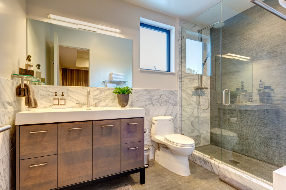 Idéer för funkis vitt badrum med dusch, med släta luckor, skåp i mellenmörkt trä, en dusch i en alkov, en toalettstol med hel cisternkåpa, grå kakel, vita väggar, ett integrerad handfat, grått golv och dusch med gångjärnsdörr