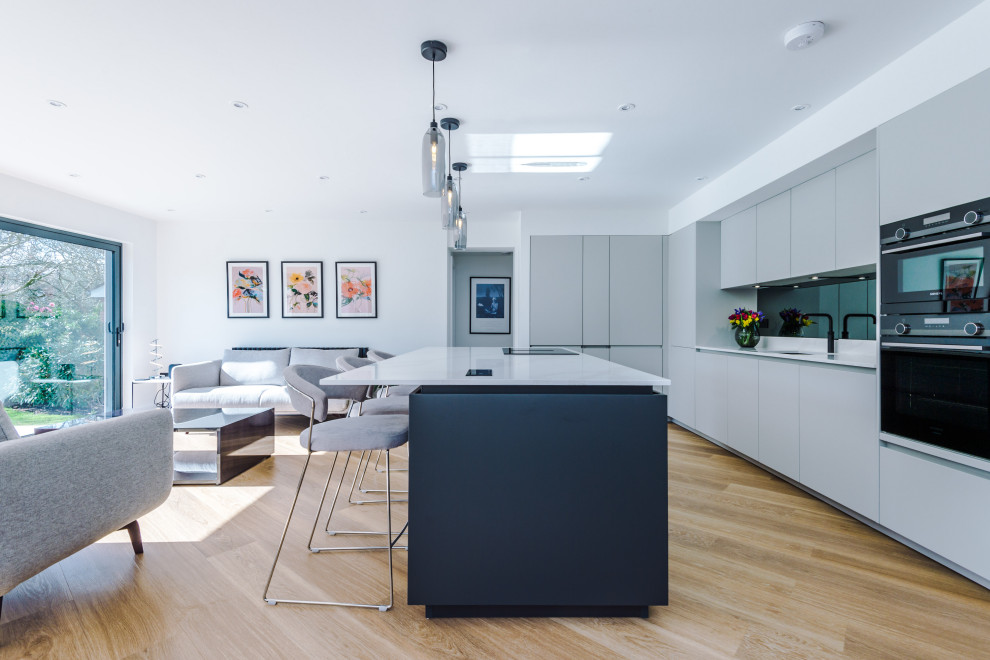 This is an example of a large modern kitchen in Manchester with an integrated sink, flat-panel cabinets, quartzite benchtops, metallic splashback, glass sheet splashback, stainless steel appliances and with island.