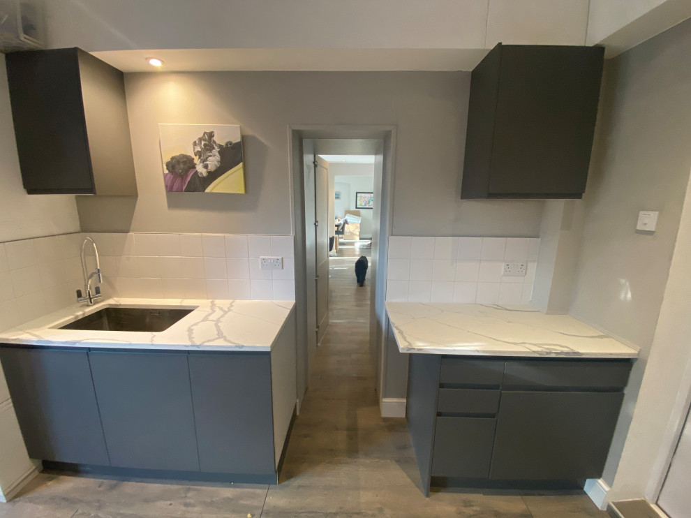 Design ideas for a large contemporary galley utility room in London with a drop-in sink, flat-panel cabinets, grey cabinets, quartzite benchtops, white splashback, porcelain splashback, beige walls, laminate floors, a side-by-side washer and dryer, grey floor and multi-coloured benchtop.