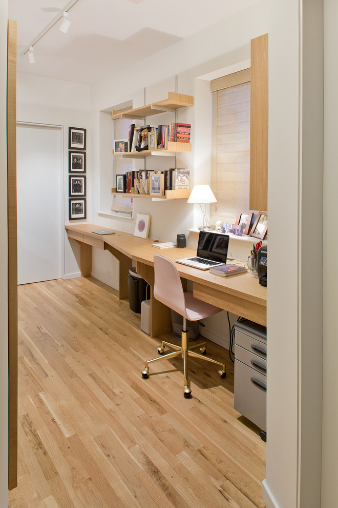 Inspiration for a mid-sized contemporary home office in New York with white walls, light hardwood floors, a built-in desk, brown floor and no fireplace.