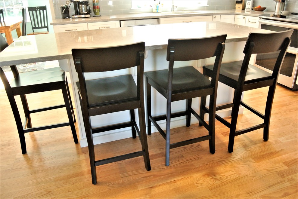 Example of a transitional light wood floor kitchen design in Boston with an undermount sink, shaker cabinets, white cabinets, quartz countertops, gray backsplash, subway tile backsplash, stainless steel appliances, an island and gray countertops