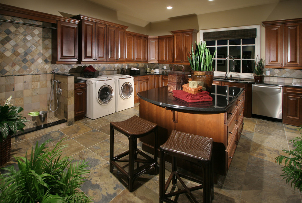 Photo of an expansive traditional utility room in Denver with an undermount sink, raised-panel cabinets, medium wood cabinets, granite benchtops, beige walls, slate floors and a side-by-side washer and dryer.