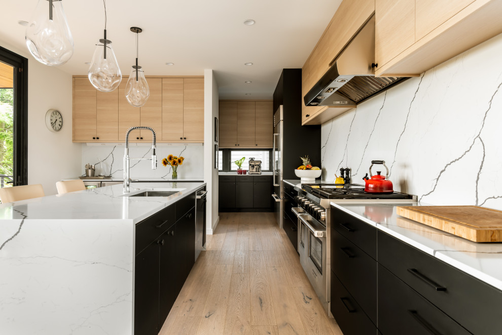 Bild på ett mellanstort funkis vit vitt kök, med släta luckor, svarta skåp, bänkskiva i kvarts, vitt stänkskydd, rostfria vitvaror, ljust trägolv och en köksö