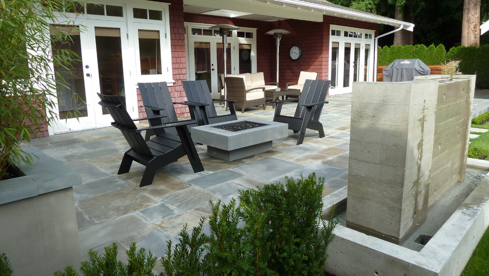 Mid-sized arts and crafts backyard patio in Vancouver with a fire feature, natural stone pavers and a roof extension.