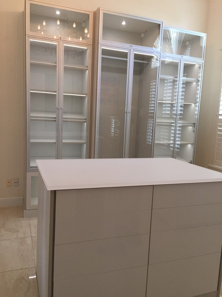 This is an example of a large modern gender-neutral walk-in wardrobe in Orlando with glass-front cabinets and limestone floors.