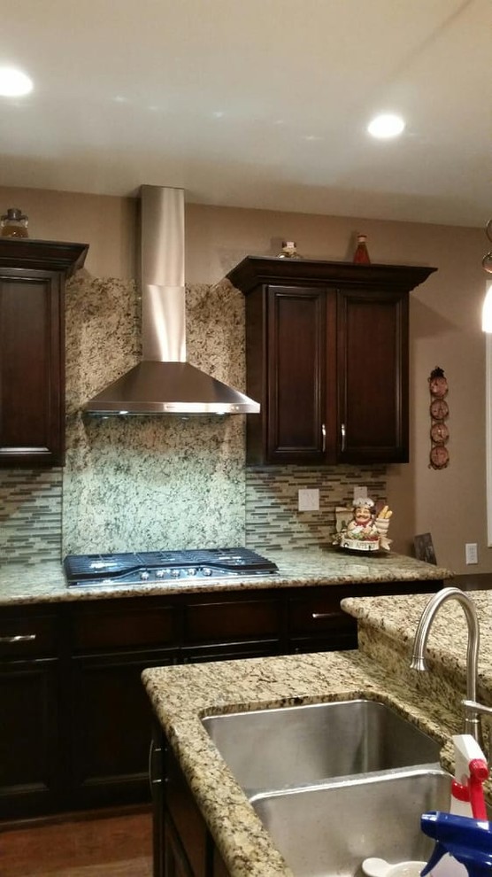 Example of a mid-sized transitional l-shaped medium tone wood floor and brown floor open concept kitchen design in Los Angeles with a double-bowl sink, recessed-panel cabinets, brown cabinets, granite countertops, beige backsplash, matchstick tile backsplash, stainless steel appliances, an island and beige countertops