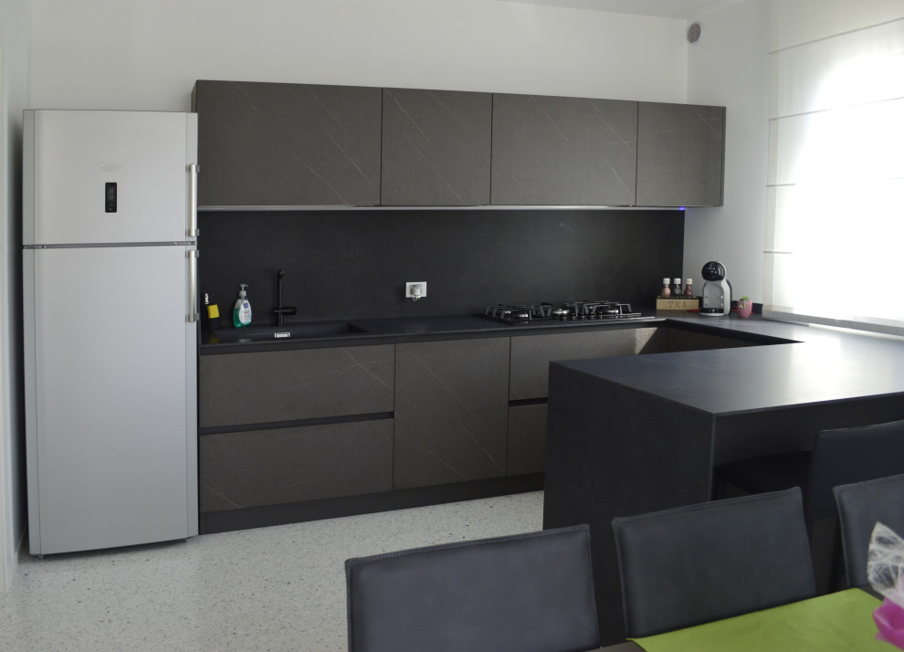 Large modern u-shaped eat-in kitchen in Other with an undermount sink, flat-panel cabinets, black cabinets, laminate benchtops, black splashback, porcelain splashback, black appliances, terrazzo floors, with island, white floor and black benchtop.
