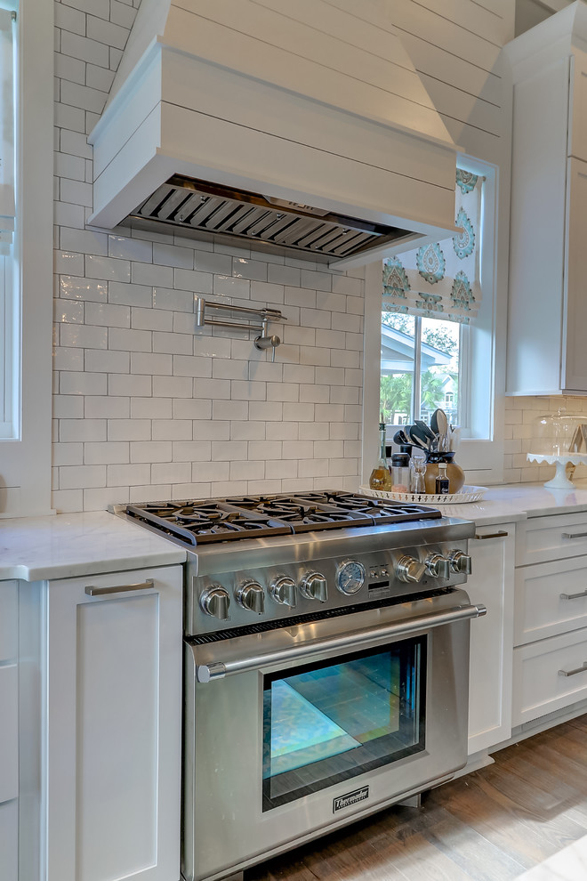 Design ideas for a large contemporary u-shaped open plan kitchen in Charleston with white cabinets, marble benchtops, white splashback, glass tile splashback, stainless steel appliances, light hardwood floors, with island and brown floor.