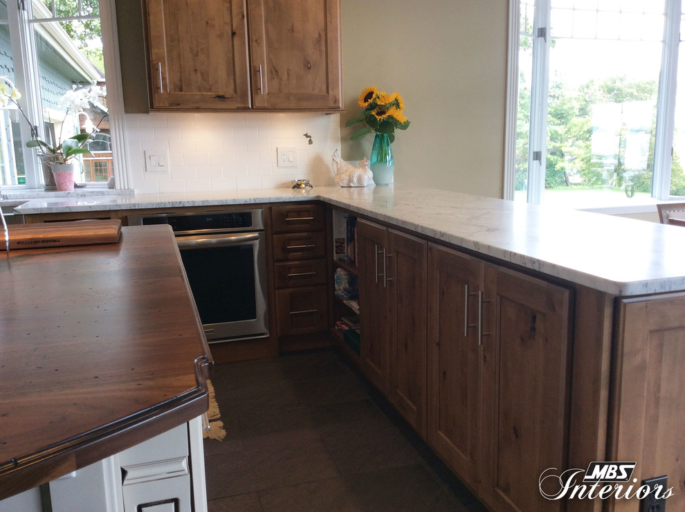 Inspiration for a mid-sized transitional u-shaped ceramic tile and gray floor eat-in kitchen remodel with a farmhouse sink, recessed-panel cabinets, medium tone wood cabinets, marble countertops, white backsplash, subway tile backsplash, stainless steel appliances and an island