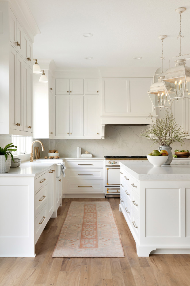 Design ideas for an expansive traditional u-shaped eat-in kitchen in Minneapolis with a farmhouse sink, recessed-panel cabinets, white cabinets, quartz benchtops, white splashback, engineered quartz splashback, white appliances, light hardwood floors, with island, brown floor and white benchtop.