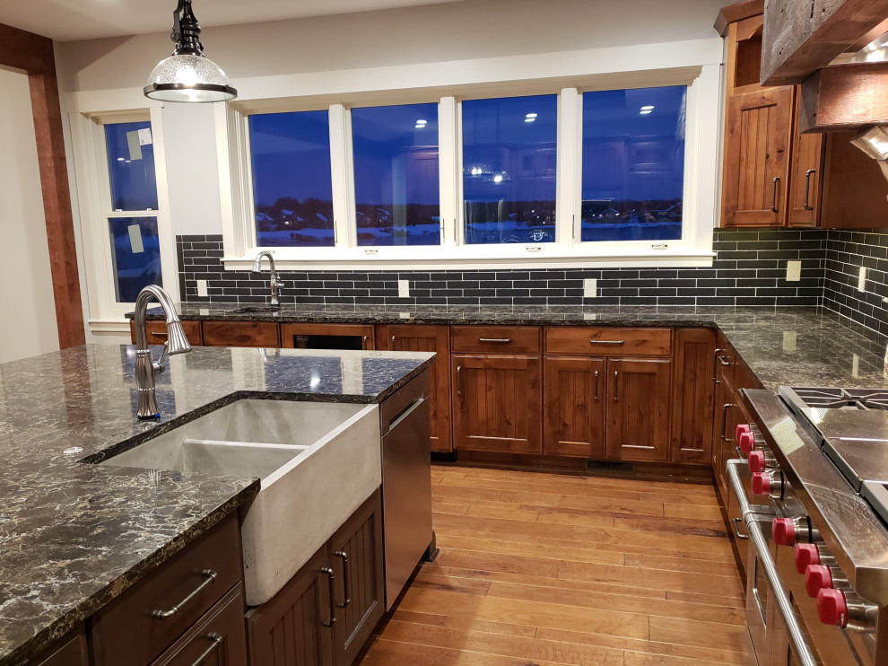 Inspiration for a rustic medium tone wood floor kitchen remodel with a farmhouse sink, recessed-panel cabinets, dark wood cabinets, quartz countertops, black backsplash, travertine backsplash, stainless steel appliances, an island and brown countertops