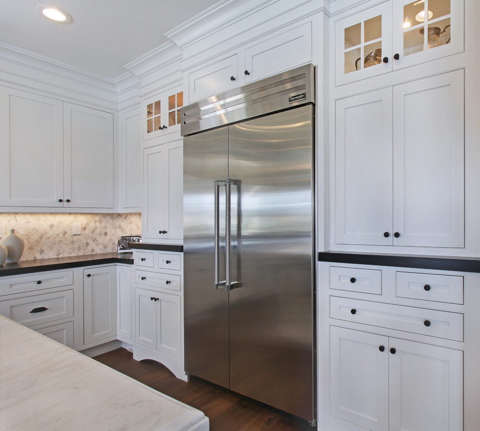 Photo of a large transitional l-shaped eat-in kitchen in Orange County with a farmhouse sink, shaker cabinets, white cabinets, quartz benchtops, white splashback, mosaic tile splashback, stainless steel appliances, medium hardwood floors and with island.
