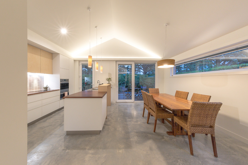 Photo of a small contemporary galley open plan kitchen in Canberra - Queanbeyan with a single-bowl sink, flat-panel cabinets, white cabinets, beige splashback, ceramic splashback, stainless steel appliances, concrete floors, with island, grey floor and brown benchtop.