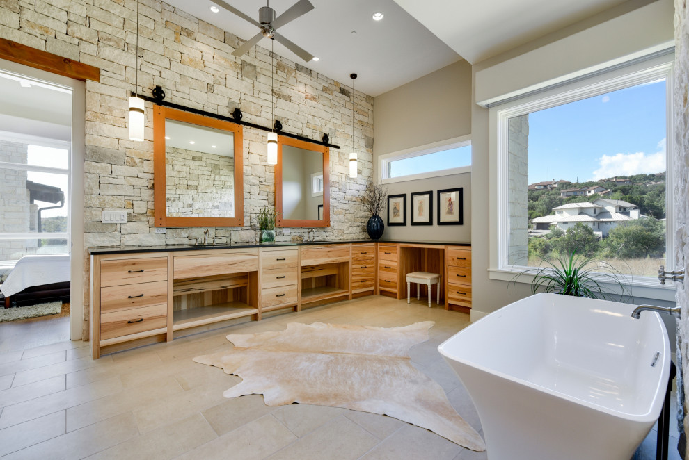 This is an example of a transitional master bathroom in Austin with flat-panel cabinets, light wood cabinets, a freestanding tub, grey walls, an undermount sink, beige floor, black benchtops, a double vanity and a built-in vanity.