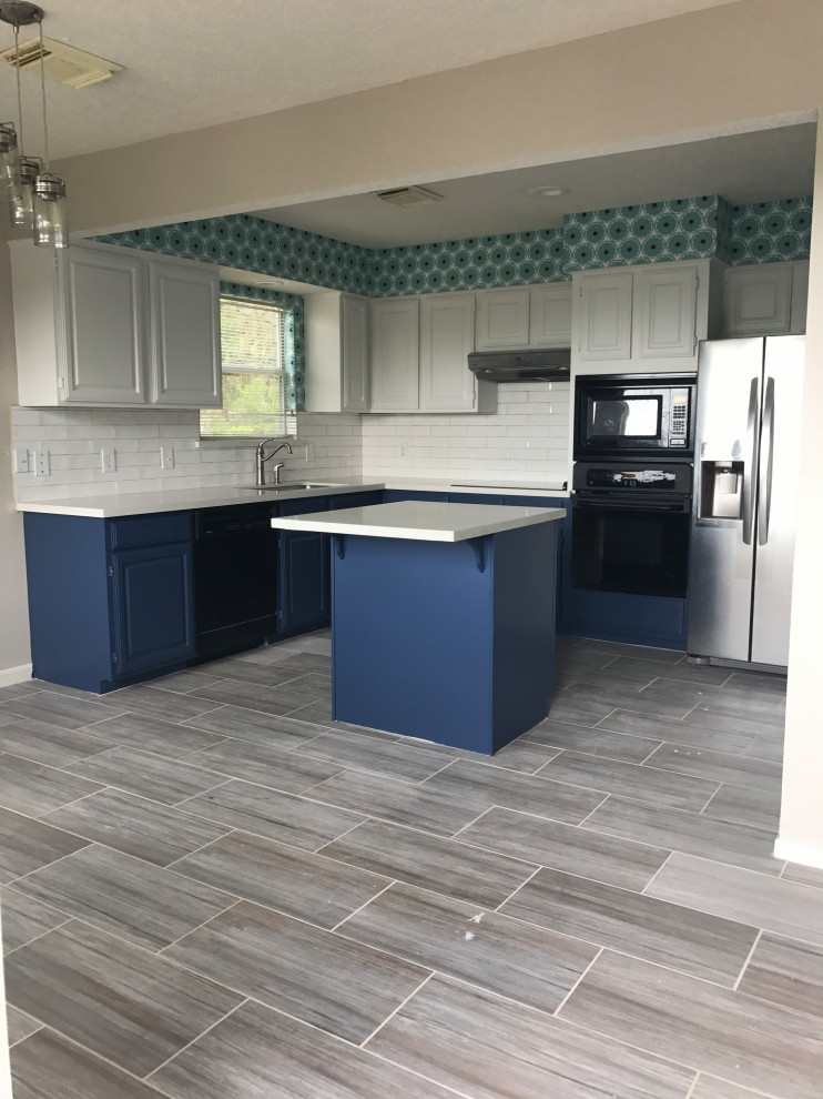 Photo of a medium sized rural l-shaped kitchen/diner in Houston with a built-in sink, flat-panel cabinets, blue cabinets, white splashback, ceramic splashback, black appliances, plywood flooring, an island, grey floors, white worktops and a drop ceiling.