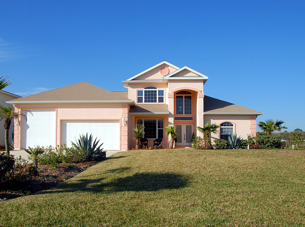 Mid-sized tropical one-storey stucco pink house exterior in Tampa with a hip roof and a shingle roof.
