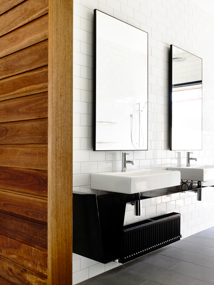 Mid-sized contemporary kids bathroom in Melbourne with open cabinets, black cabinets, a drop-in tub, an open shower, a wall-mount toilet, white tile, subway tile, white walls, ceramic floors, a wall-mount sink and stainless steel benchtops.