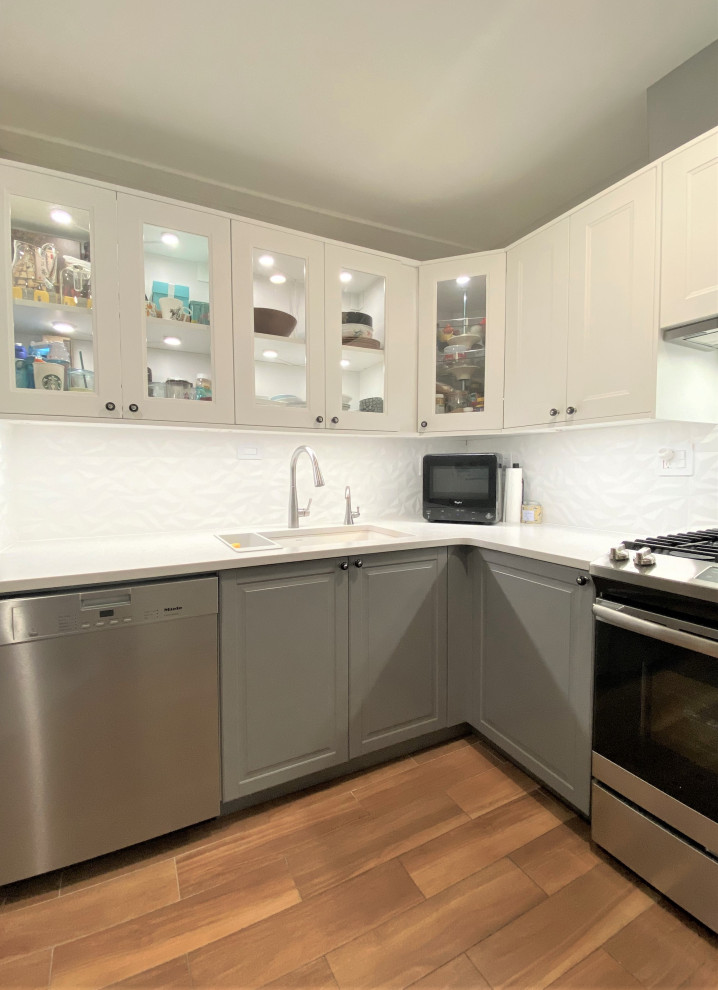Mid-sized transitional u-shaped ceramic tile and brown floor enclosed kitchen photo with an undermount sink, shaker cabinets, gray cabinets, quartzite countertops, white backsplash, porcelain backsplash, stainless steel appliances, no island and gray countertops