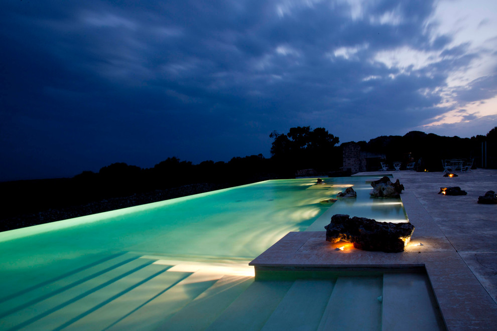 This is an example of an expansive mediterranean backyard rectangular infinity pool in Rome with a pool house.
