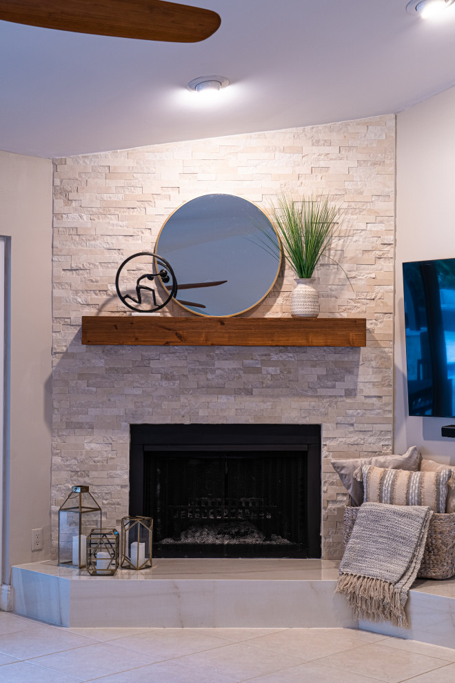 Modelo de sala de estar abierta marinera de tamaño medio con paredes beige, chimenea de esquina, marco de chimenea de piedra, televisor colgado en la pared y suelo beige