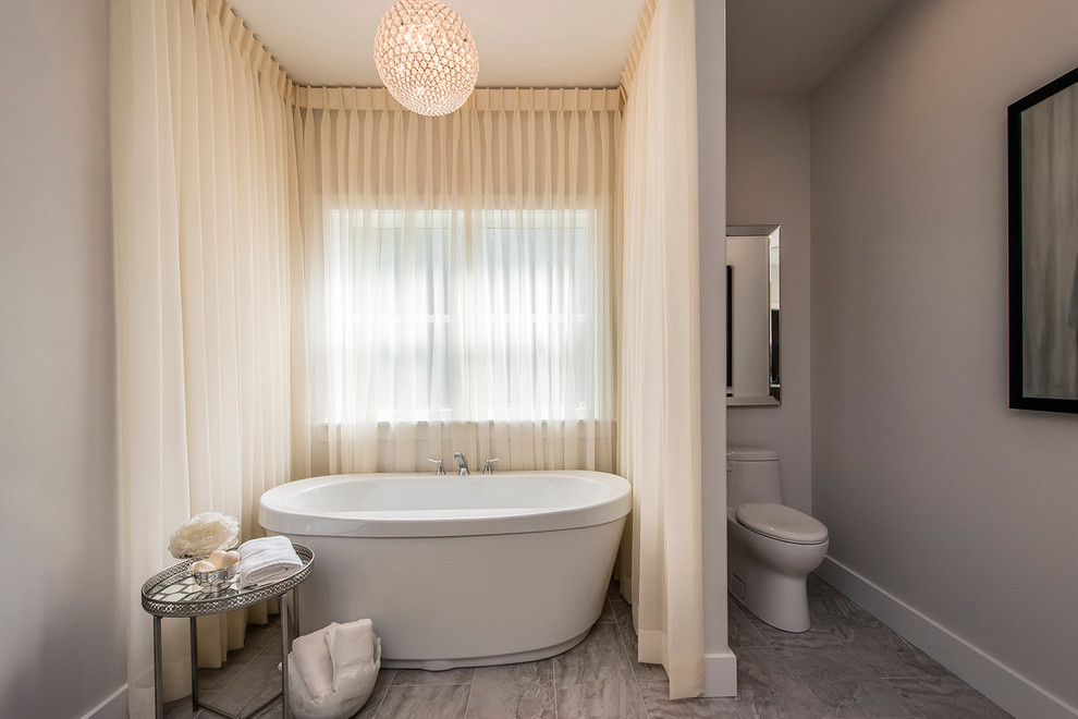 Example of a mid-sized transitional master gray tile and porcelain tile porcelain tile and beige floor freestanding bathtub design with flat-panel cabinets, dark wood cabinets, white walls, a drop-in sink, quartzite countertops and a one-piece toilet
