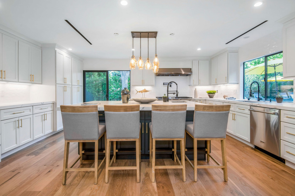 Transitional u-shaped medium tone wood floor and brown floor enclosed kitchen photo in Los Angeles with an undermount sink, shaker cabinets, white cabinets, white backsplash, subway tile backsplash, stainless steel appliances, an island and multicolored countertops