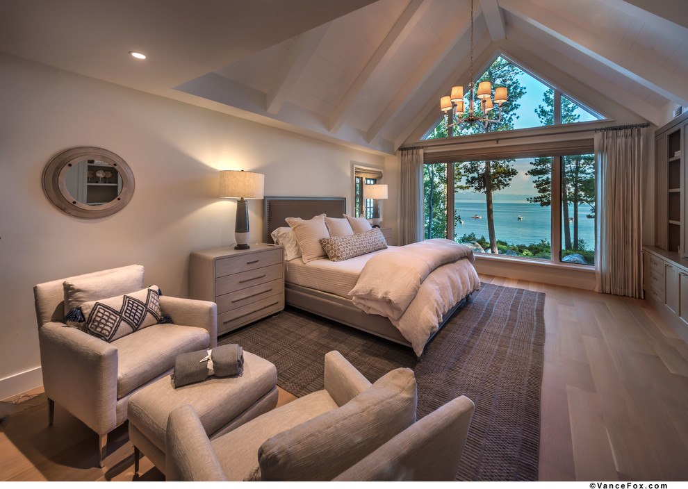 Large beach style master bedroom in Other with white walls, medium hardwood floors, a two-sided fireplace, a wood fireplace surround and beige floor.