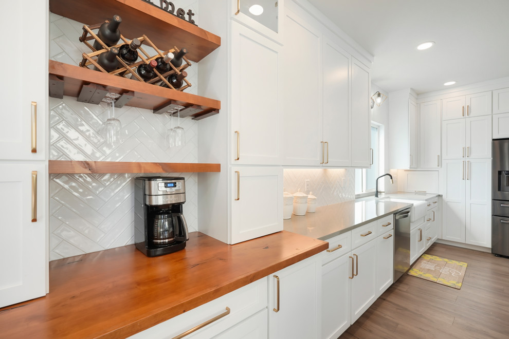 Open concept kitchen - large transitional l-shaped open concept kitchen idea in Denver with a farmhouse sink, shaker cabinets, white cabinets, quartz countertops, white backsplash, ceramic backsplash, stainless steel appliances, an island and gray countertops