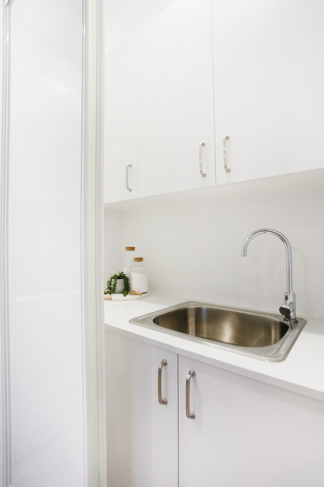 This is an example of a small contemporary galley dedicated laundry room in Sunshine Coast with a drop-in sink, flat-panel cabinets, light wood cabinets, quartz benchtops, white walls, light hardwood floors, a stacked washer and dryer and white benchtop.