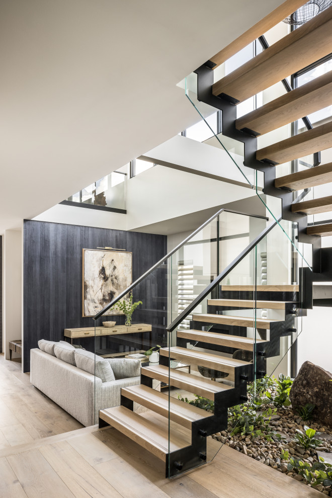 This is an example of a large contemporary wood u-shaped staircase in Sydney with metal risers and glass railing.