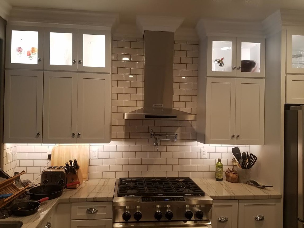 Example of a large transitional u-shaped porcelain tile and brown floor enclosed kitchen design in Los Angeles with an undermount sink, shaker cabinets, white cabinets, quartzite countertops, white backsplash, subway tile backsplash, stainless steel appliances, an island and multicolored countertops