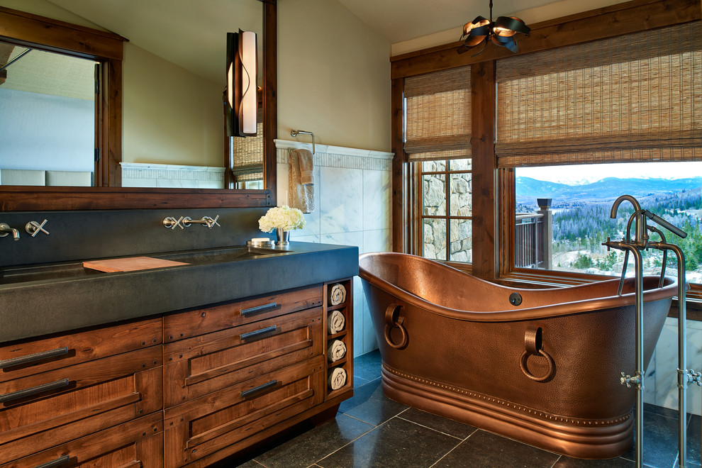 Country master bathroom in Denver with an integrated sink, medium wood cabinets, concrete benchtops, a freestanding tub, an open shower, a two-piece toilet, white tile, stone tile, beige walls and limestone floors.