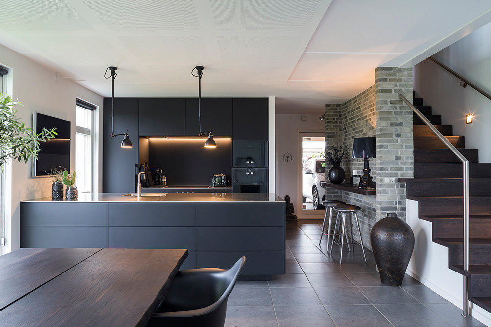 Inspiration for a contemporary eat-in kitchen in Other with flat-panel cabinets, black cabinets, an integrated sink, stainless steel benchtops, black splashback, black appliances, a peninsula and grey floor.