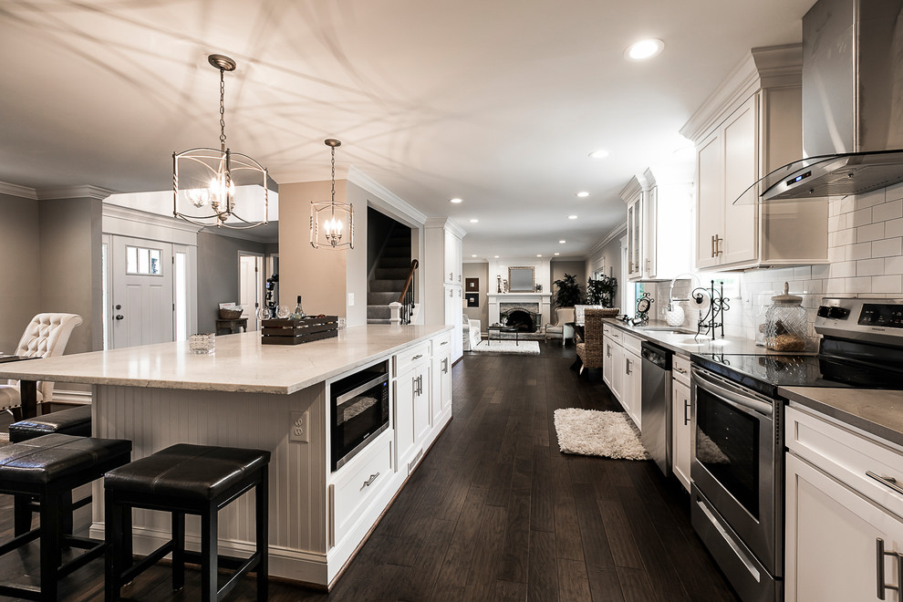Eat-in kitchen - transitional galley dark wood floor and brown floor eat-in kitchen idea in Baltimore with an undermount sink, white cabinets, quartz countertops, white backsplash, subway tile backsplash, stainless steel appliances, an island, white countertops and recessed-panel cabinets